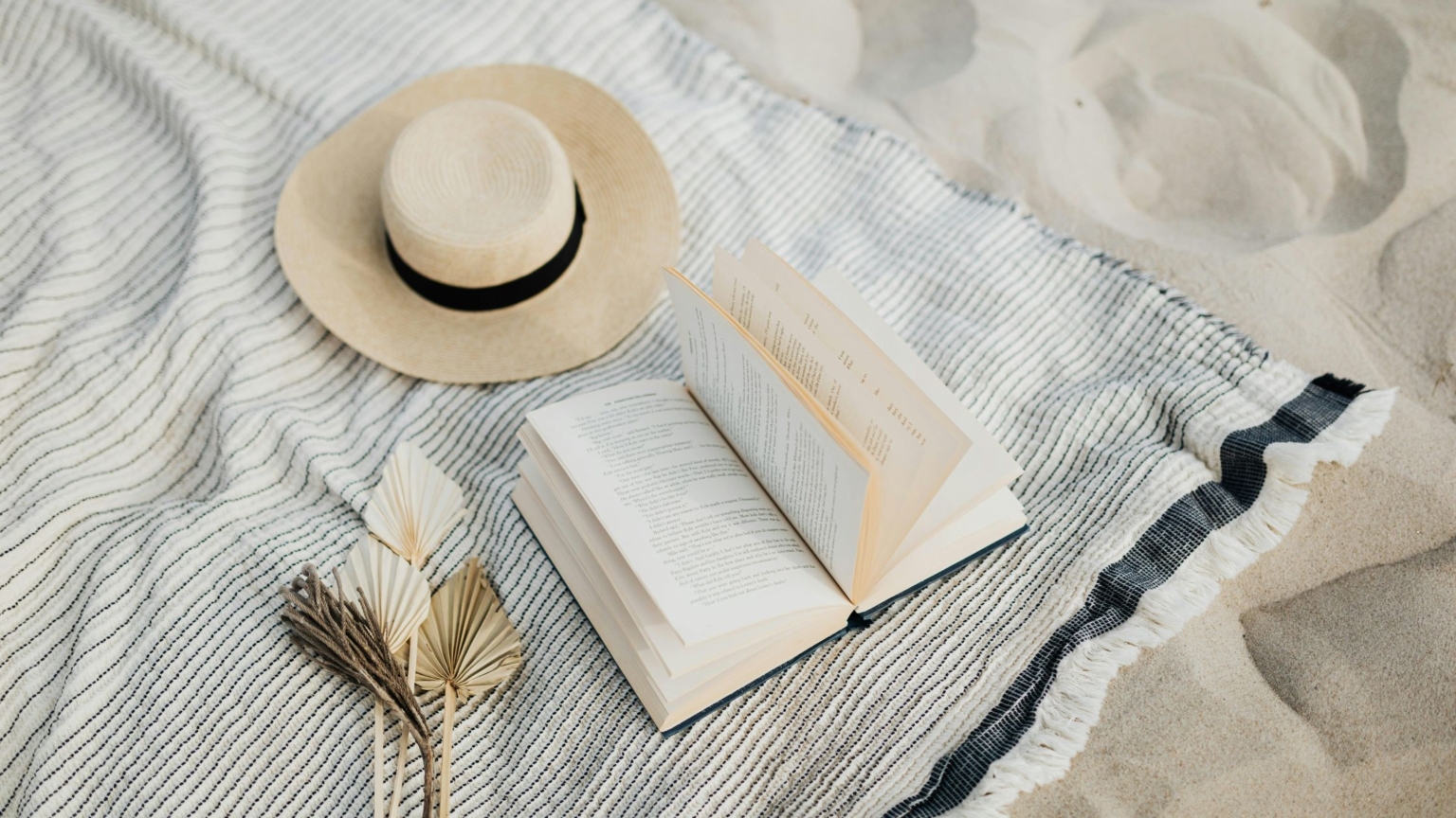 beach scene with book and beach hat on white sand
